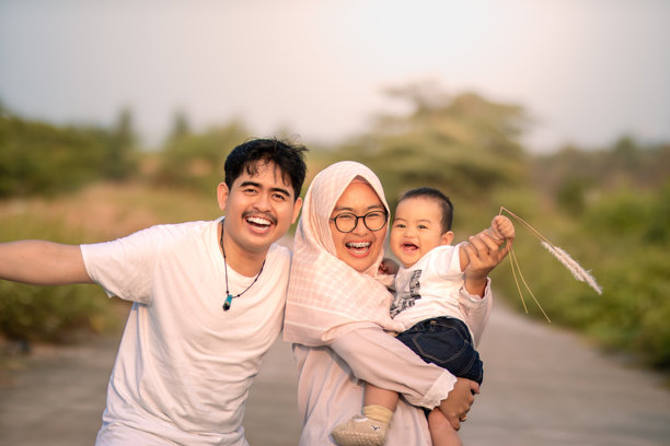 一家看起来幸福的家庭，母亲、父亲和小男孩欢声笑语，大家面向镜头开心地笑着。照片中的自然氛围宁静而美丽。图片下载