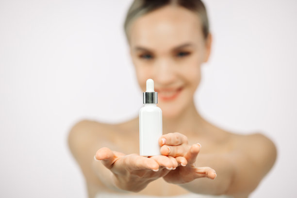 一位皮肤保养良好的女性在白色背景下使用精华液。这张图片展示了护肤，强调通过使用透明质酸来实现滋润和美丽。图片下载