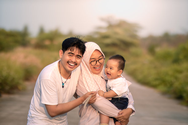 一家看起来幸福的家庭，充满欢声笑语，母亲、父亲和婴儿男孩在一起。婴儿男孩对爸爸笑。照片中的自然氛围宁静而美丽。图片下载