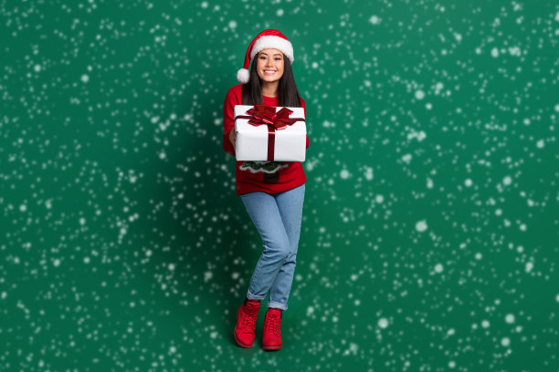穿着红色丑陋印花圣诞毛衣的可爱时尚女士在绿色背景前送你礼物的全身照片图片下载