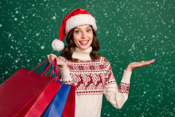 拿着包裹，手臂指向空白区域，展示新年优惠的漂亮女士照片，绿色背景图片下载