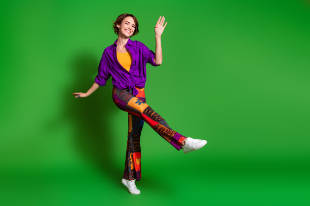 穿着紫色时尚衬衫、复古裤子和棕色波波头的时髦女性在绿色背景上跳舞的照片肖像图片下载