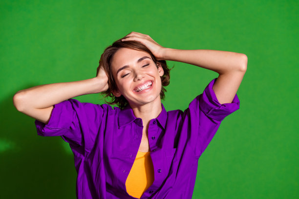 年轻迷人的女孩肖像照片，棕色头发，触摸头部，幸福的一天，穿着紫色衬衫，背景为绿色。图片下载