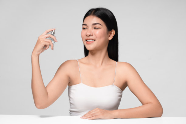 手持香水的女性。完美妆容的女性照片，背景为灰色。美容概念。图片下载