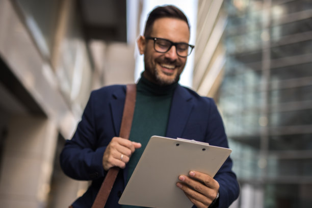 一位英俊、微笑、穿着得体的中年男士正前往工作，手中拿着公文包，背景是一座现代建筑。这张照片捕捉了快节奏的生活方式和商业时刻。图片下载