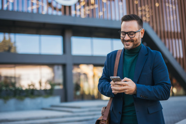 一位英俊、微笑、穿着得体的中年男士正前往工作，手中拿着公文包，背景是一座现代建筑。这张照片捕捉了快节奏的生活方式和商业时刻。图片下载