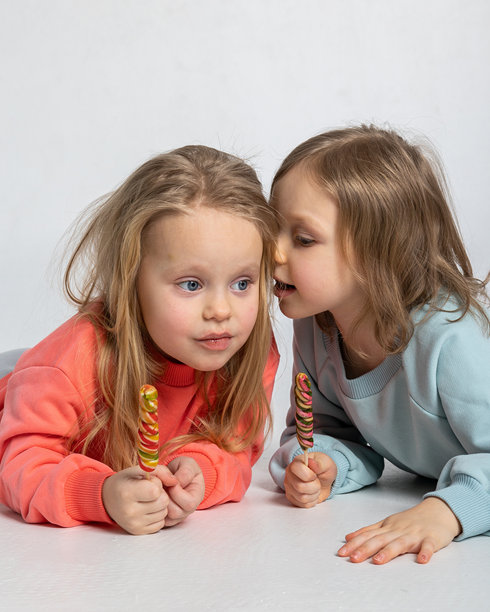 两位可爱的小女孩手中拿着糖果棒，背景明亮。竖版照片。图片下载