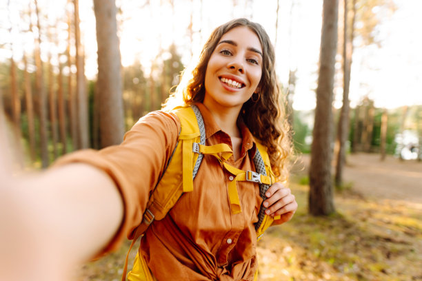 在大自然中自拍。美丽的女人在阳光明媚的森林中散步时拍摄自己的照片。图片下载