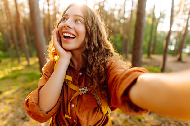 在大自然中自拍。美丽的女人在阳光明媚的森林中散步时拍摄自己的照片。图片下载