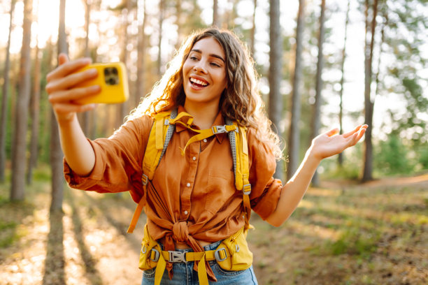 在大自然中自拍。美丽的女人在阳光明媚的森林中散步时拍摄自己的照片。图片下载