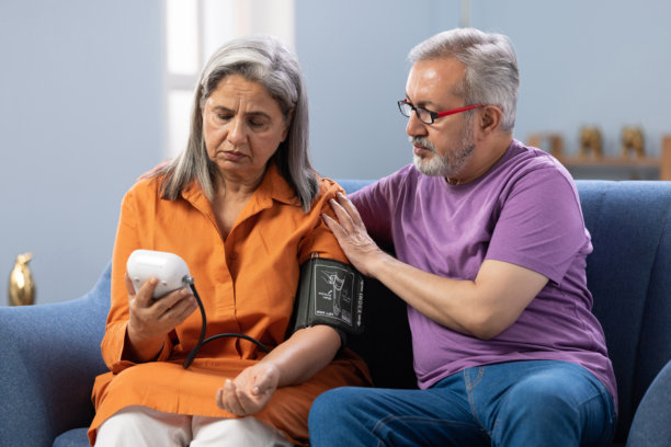 老年夫妇在家中沙发上使用医疗设备测量血压，注意健康库存照片图片下载