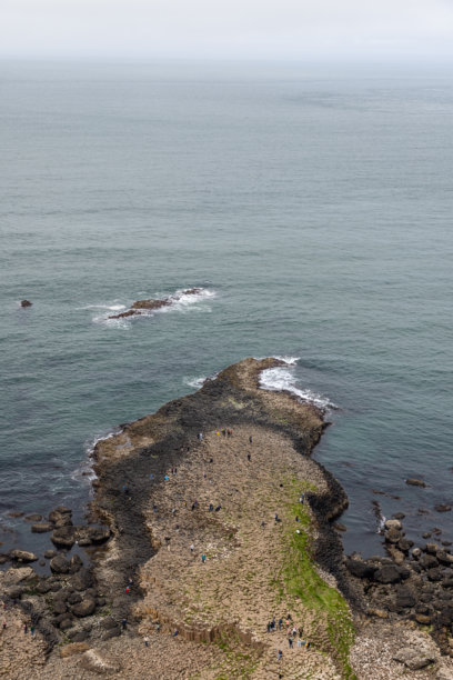 巨人之路的鸟瞰图，游客在著名的玄武岩柱上行走。竖版照片捕捉了独特的地质构造和宁静的海面。图片下载