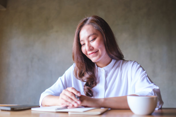 一位女性在木桌上写笔记，旁边有手机和咖啡杯的肖像照片图片下载