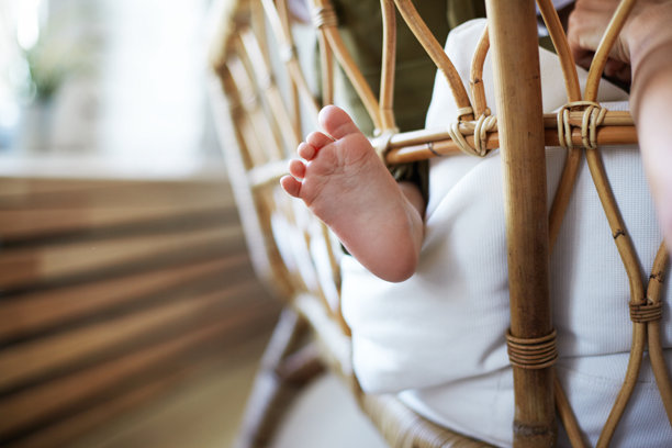 婴儿期、育儿、父母身份、母性和纯真概念。室内编织椅上睡着的新生儿横向照片。特写视角下，宝宝的脚从毯子外露。图片下载