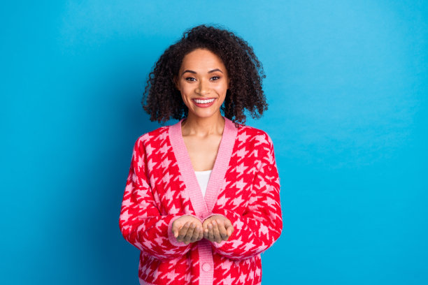 一位美丽的美国女孩，卷发，穿着红色时尚开衫，手持免费送货优惠，背景为蓝色。图片下载