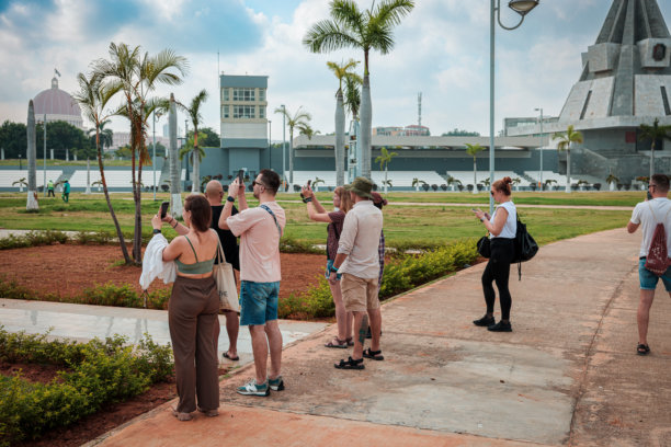 游客在罗安达安哥拉的阿戈斯蒂纽·内托纪念馆拍摄纪念照片，周围环绕着茂盛的绿色植物和引人注目的建筑图片下载