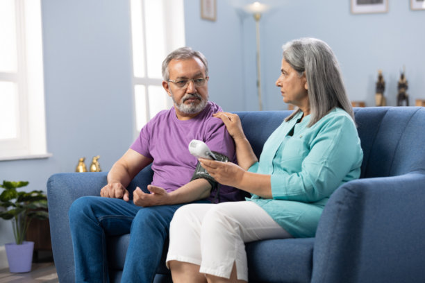 老年夫妇在家中沙发上使用医疗设备测量血压，注意健康库存照片图片下载