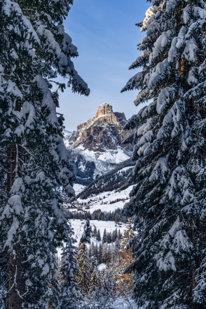 被积雪覆盖的树木框住的萨松赫峰，耸立在意大利多洛米蒂山脉一个宁静的冬季山谷上。雪白的景色和远处的村庄构成了宁静的阿尔卑斯风光。（竖版照片）图片下载