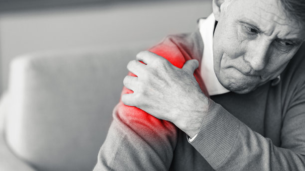 黑白照片：坐在沙发上，触摸疼痛肩膀的老年男人图片下载