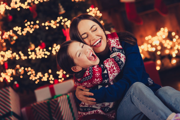 可爱的家庭照片，母亲和小女儿在室内温馨地拥抱，穿着节日的圣诞服装，洋溢着传统的节日气氛。图片下载