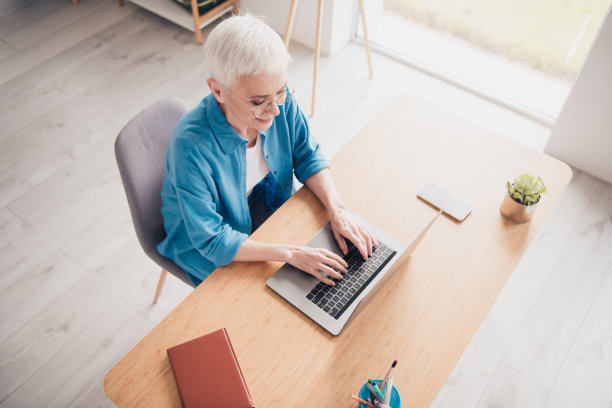 高角度拍摄的优雅老年女士在现代室内家居办公室公寓中穿着衬衫使用笔记本电脑的照片图片下载