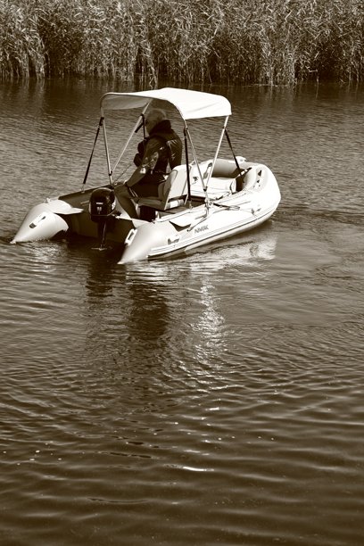 波兰索比耶舍沃 - 2024年7月21日：一位老人驾驶着一艘摩托艇，水中映出他的倒影，照片为褐色调。图片下载