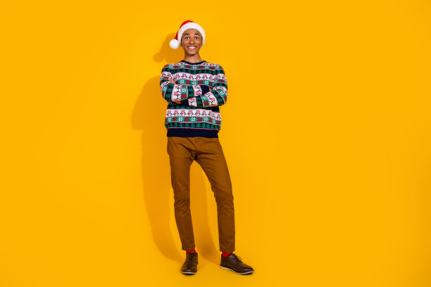 年轻男士自信地交叉双手，穿着节日圣诞服装，在黄色背景下庆祝冬季假期的全身照片图片下载