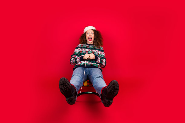 漂亮年轻女性在红色背景下骑雪橇，庆祝圣诞节的全身照片图片下载