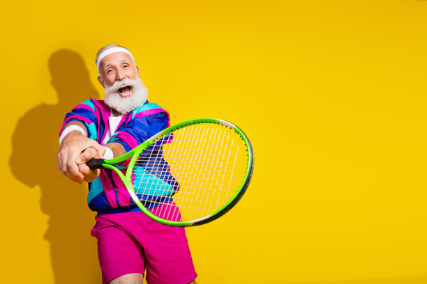 穿着时尚复古运动服的快乐老人在黄色背景下兴奋地打网球的照片横幅图片下载