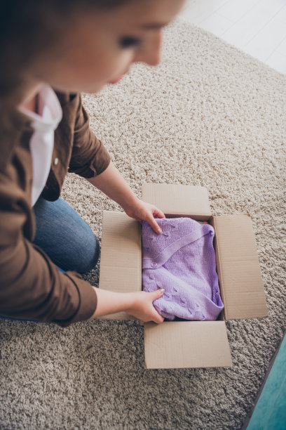 年轻女子将衣服装入纸箱的特写照片，在舒适的阁楼现代住宅内出售旧衣柜，坐在地板上图片下载