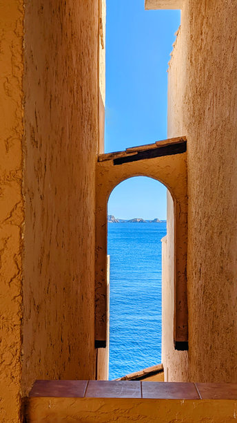 马略卡岛典型建筑的垂直几何照片，橙色墙壁与拱形结构，蓝色海洋与天际线中的天空相接。图片下载