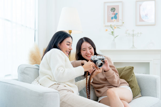 美丽的亚洲女性近距离侧面视图，愉快地一起看相机拍摄的照片，坐在客厅里。图片下载