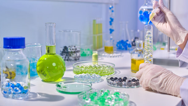 水凝胶实验照片，研究人员正在用移液管将黄色精华滴入装有透明胶球的量筒中。正面视图，留有空白空间供设计使用。图片下载