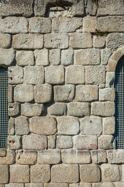 这张照片展示了一堵古老石墙的特写，可能是波尔图某个历史建筑的一部分。墙面由大块不规则的石头构成，每块石头都被时间侵蚀，缝隙中长出小片植被。图片下载