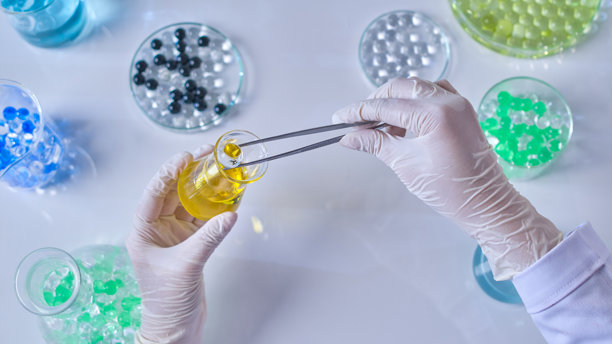 科学家的手戴着医用手套，从小型锥形瓶中取出一个透明的胶球。广告照片是从顶部拍摄的。图片下载