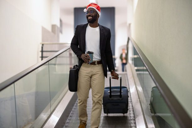 带着行李箱和圣诞老人帽的男子在扶梯上旅行图片下载