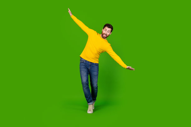 全身照片：年轻帅气的男性在绿色背景上穿着时尚的黄色服装，双手张开保持平衡走在绳索上。图片下载