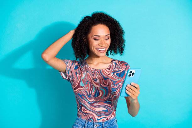 漂亮年轻女孩的照片肖像，手持设备，触摸头部，穿着时尚多彩的衣服，背景为水绿色。图片下载