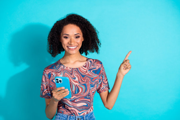 漂亮年轻女孩的照片肖像，手持设备指向空白处，穿着时尚多彩的衣服，背景为水绿色。图片下载