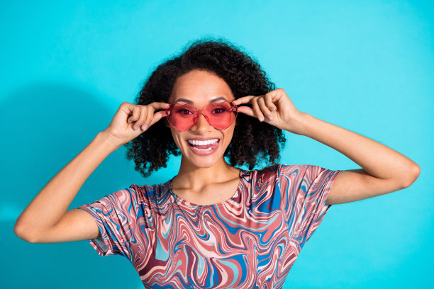漂亮年轻女孩的照片肖像，戴着太阳镜，吐着舌头，穿着时尚多彩的衣服，背景为水绿色。图片下载