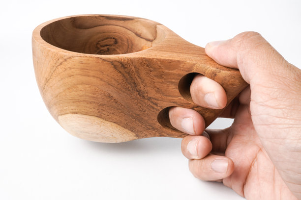 特写照片，男人手持木制库克萨杯或古克西杯，杯子有两个手指握孔，背景为白色。30度角拍摄设置。图片下载