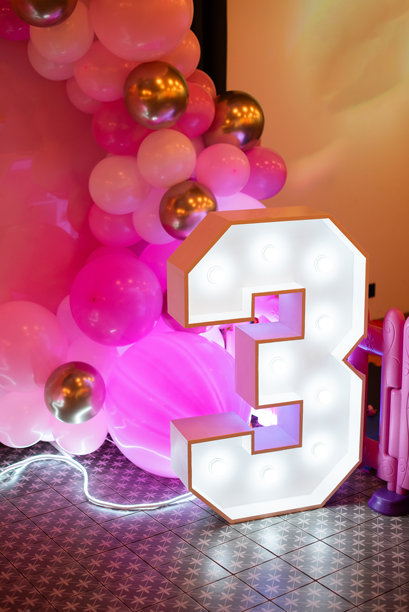 霓虹数字三，装饰着粉色和金色气球。三岁女孩的生日背景照片墙区域。生日派对的接待区。图片下载