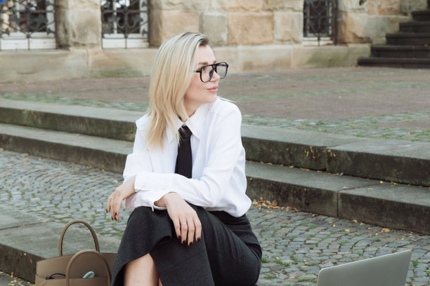 年轻的金发女性穿着商务服装，坐在街道的台阶上，手里拿着一台笔记本电脑。高质量照片。图片下载