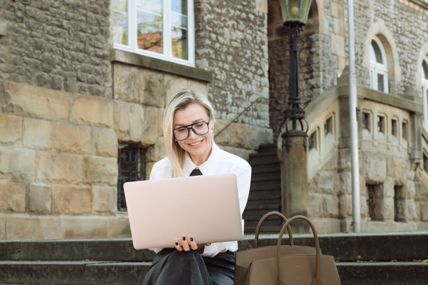 穿着商务服装的年轻女性在街上使用笔记本电脑。学习，工作。高质量照片图片下载