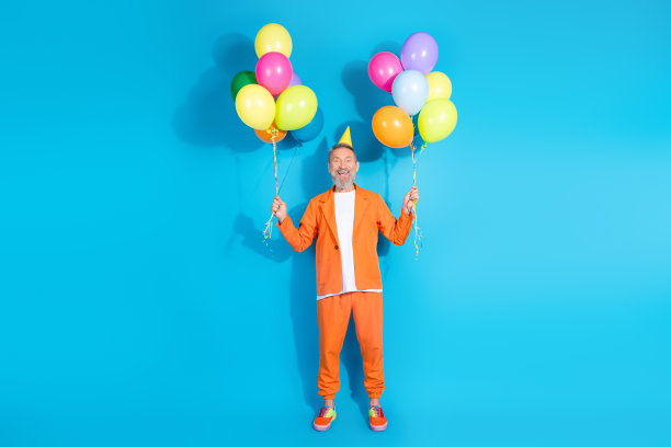 时尚的中年男子穿着橙色服装，手持气球，背景为蓝色，照片为全身照。图片下载