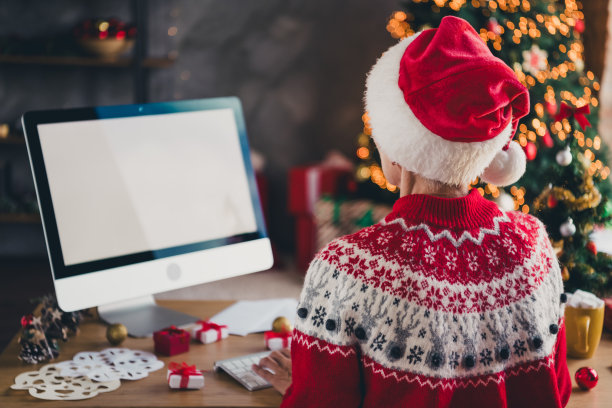 穿着毛衣的老年女性在室内公寓中使用电脑，背面照片，屏幕空白，营造圣诞节的节日气氛。图片下载