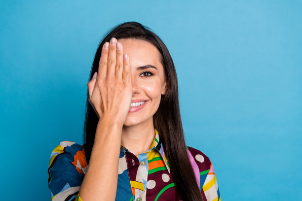 可爱年轻女性的照片肖像，遮住眼睛隐藏面容，穿着时尚的彩色印花服装，背景为蓝色。图片下载