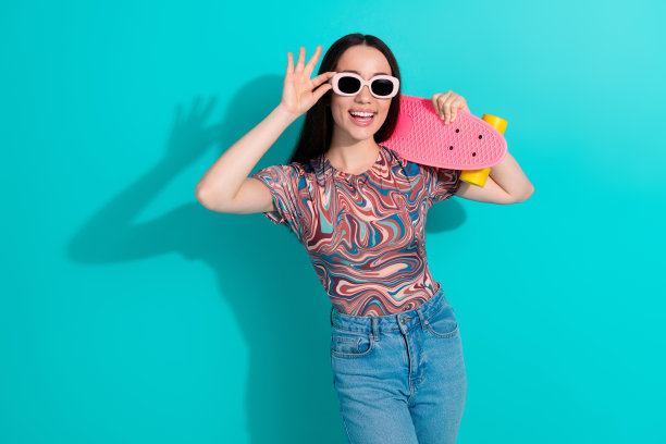 照片中可爱可爱的女孩穿着条纹t恤骑滑板，空旷的空间孤立的蓝绿色背景图片下载