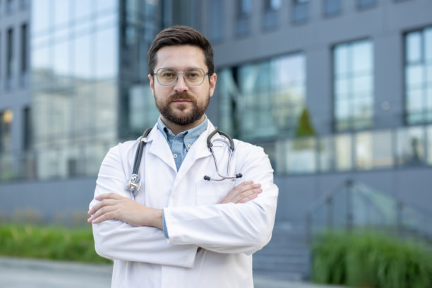 一位严肃的年轻男性医生和科学家的肖像，站在医院附近，双臂交叉在胸前，认真地看着镜头。特写照片图片下载