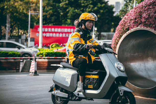 一名快递员骑着电动车穿行在中国深圳的街道上。图片下载